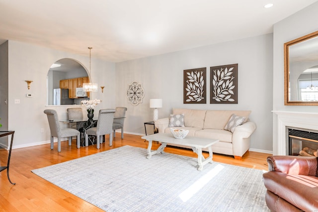 living area with arched walkways, baseboards, light wood finished floors, a glass covered fireplace, and an inviting chandelier