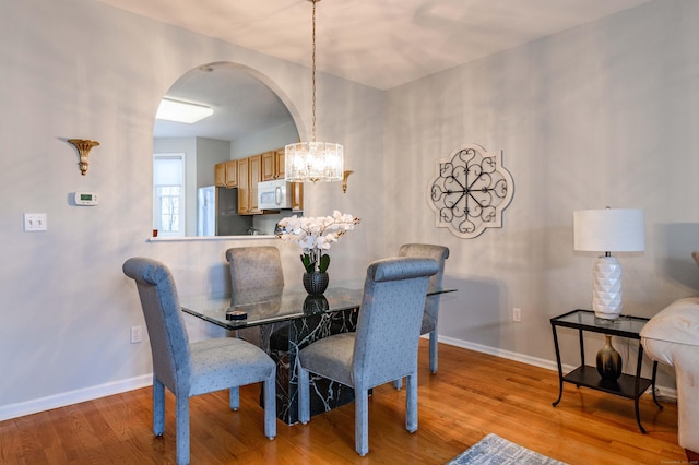 dining area featuring baseboards, a notable chandelier, arched walkways, and wood finished floors