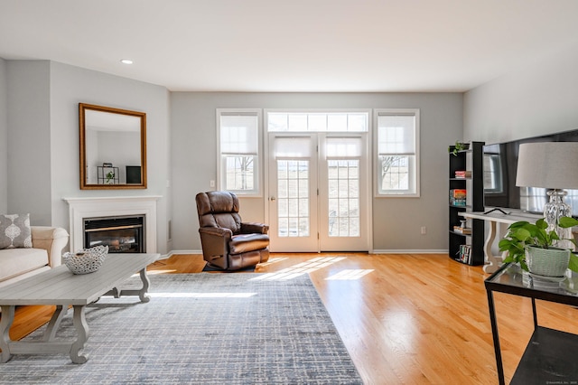 living area featuring wood finished floors, recessed lighting, a glass covered fireplace, and baseboards