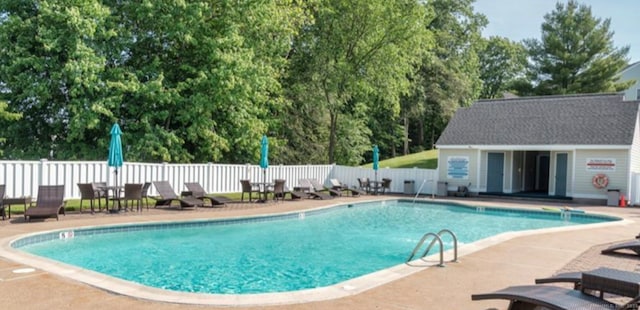 community pool with an outbuilding, a patio area, and fence