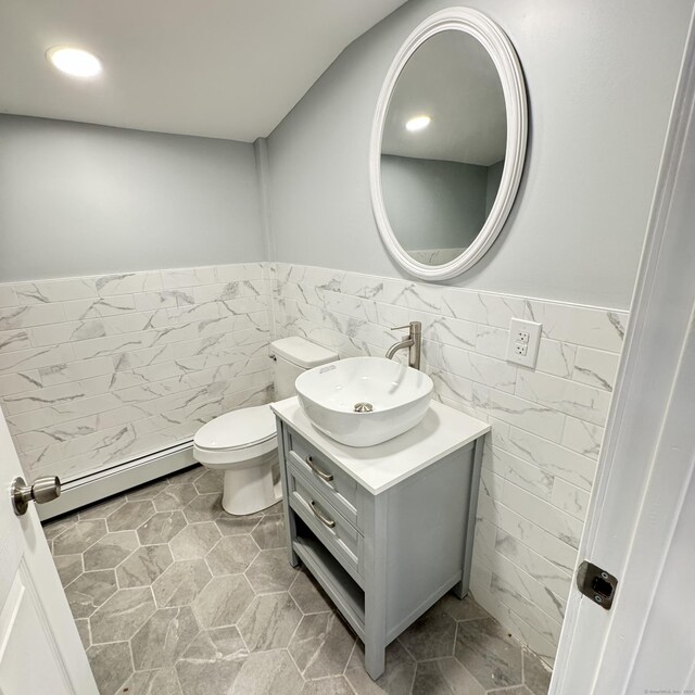 half bathroom featuring a wainscoted wall, a baseboard radiator, tile walls, and vanity