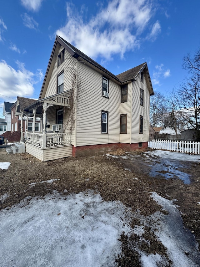 view of snowy exterior featuring covered porch and fence