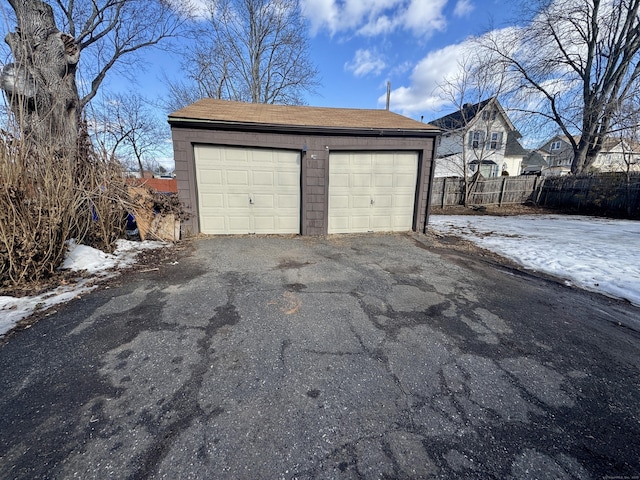 snow covered garage featuring a garage and fence