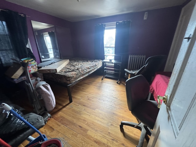 bedroom with radiator heating unit, multiple windows, and hardwood / wood-style floors