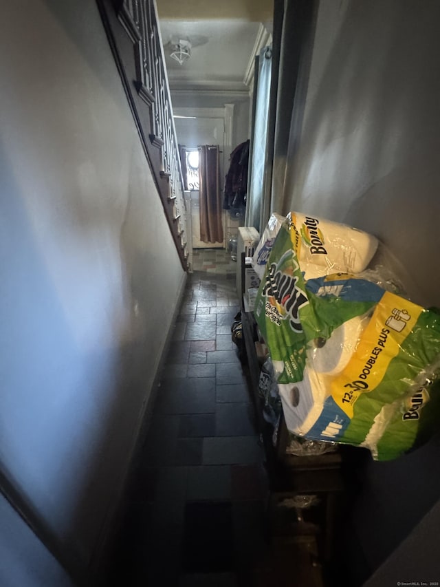 hallway with crown molding, stairs, baseboards, and stone tile flooring