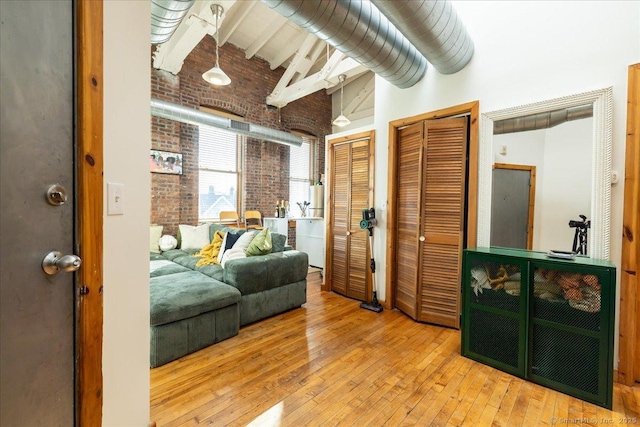 bedroom with hardwood / wood-style flooring, brick wall, a towering ceiling, multiple closets, and beamed ceiling