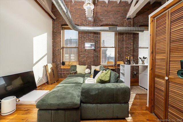 living room featuring brick wall, a towering ceiling, and hardwood / wood-style floors