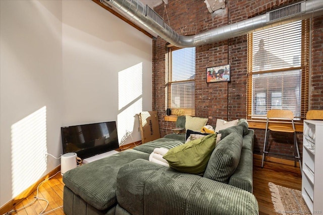 bedroom featuring visible vents, a towering ceiling, brick wall, wood finished floors, and baseboards