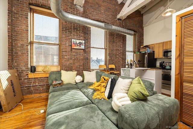 living area with brick wall, a high ceiling, and light wood-style flooring