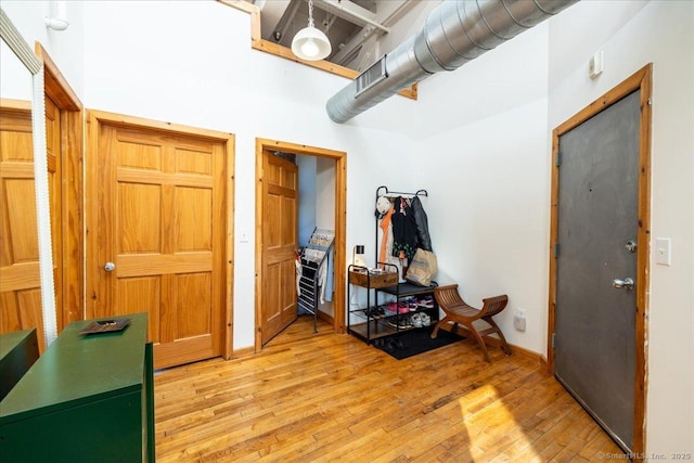 interior space featuring light wood-type flooring, baseboards, a high ceiling, and visible vents