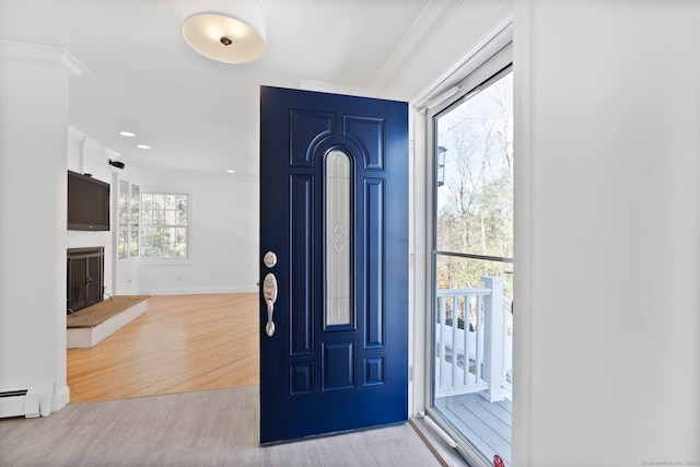 entryway featuring crown molding, baseboards, a fireplace with raised hearth, and wood finished floors