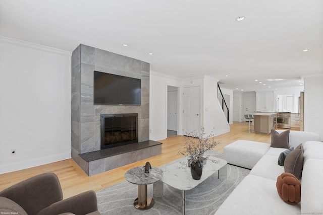 living area featuring ornamental molding, light wood finished floors, and a tiled fireplace