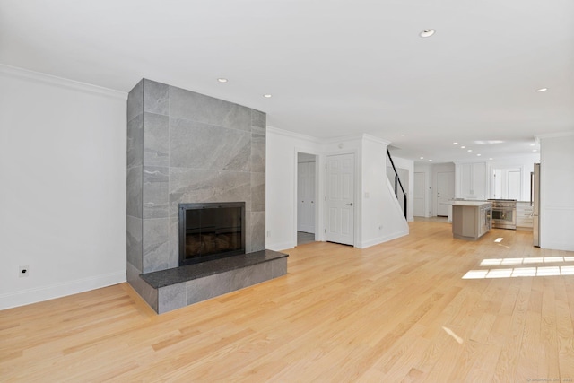 unfurnished living room with light wood-type flooring, baseboards, ornamental molding, and a tile fireplace