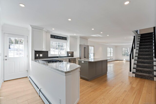 kitchen with light wood finished floors, tasteful backsplash, a kitchen island, appliances with stainless steel finishes, and a baseboard heating unit