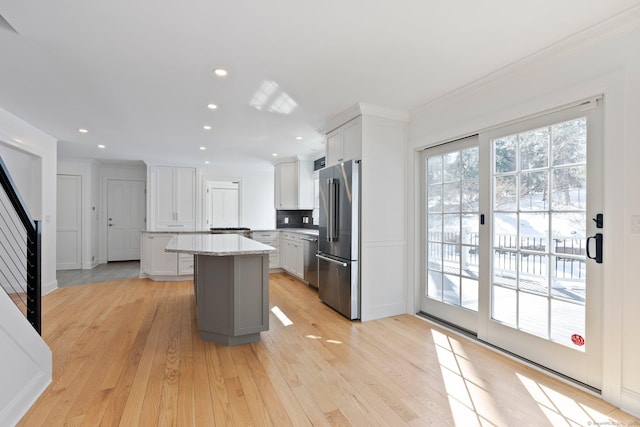 kitchen with light stone counters, a kitchen island, white cabinets, appliances with stainless steel finishes, and light wood finished floors