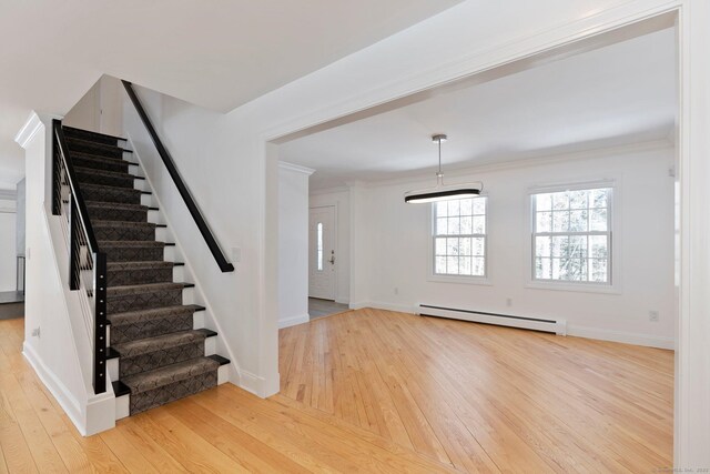 interior space with a baseboard heating unit, ornamental molding, baseboards, and hardwood / wood-style flooring