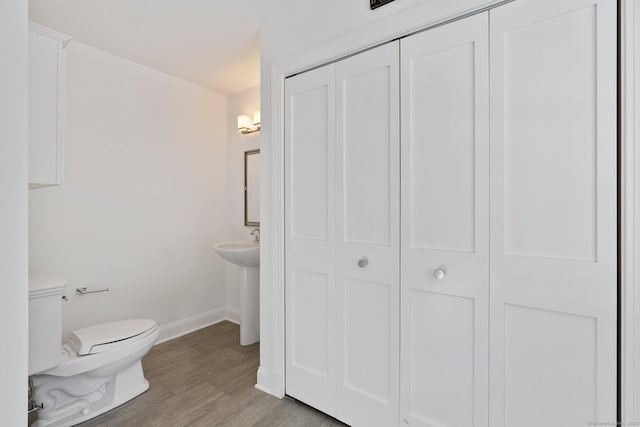 half bathroom featuring toilet, a closet, baseboards, and wood finished floors