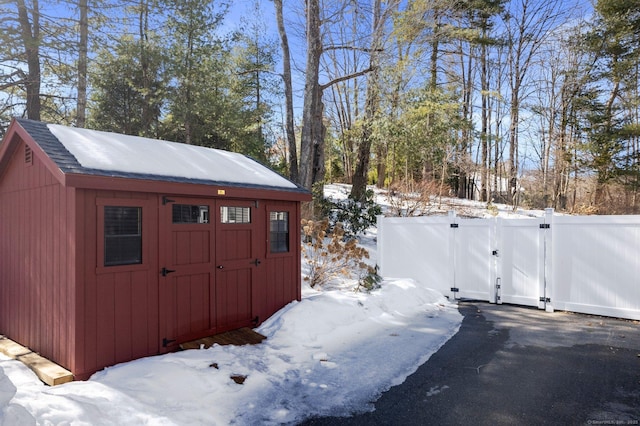 snow covered structure with a shed, an outdoor structure, and a gate