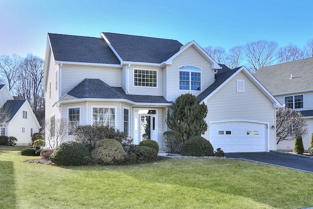 traditional-style home with a garage, driveway, a front yard, and roof with shingles