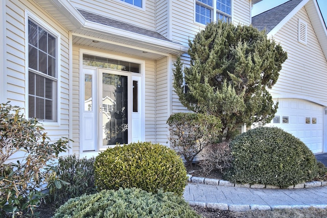 view of exterior entry with a garage and a shingled roof