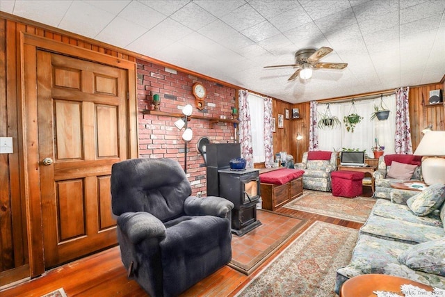 living area featuring a ceiling fan, wood finished floors, a wood stove, and wooden walls