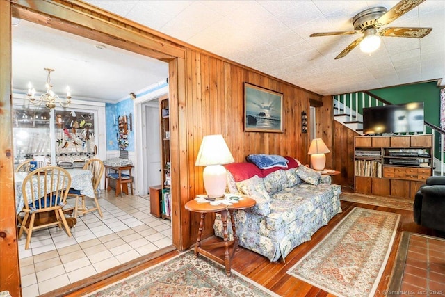 living room with ceiling fan with notable chandelier, ornamental molding, wood walls, and wood finished floors