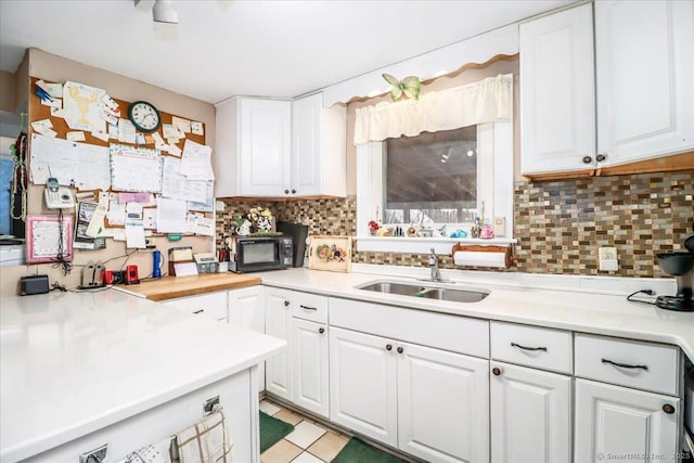 kitchen featuring light countertops, backsplash, white cabinets, a sink, and black microwave