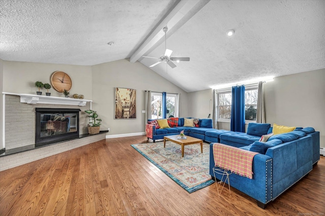 living room with lofted ceiling with beams, a textured ceiling, wood finished floors, baseboards, and a brick fireplace