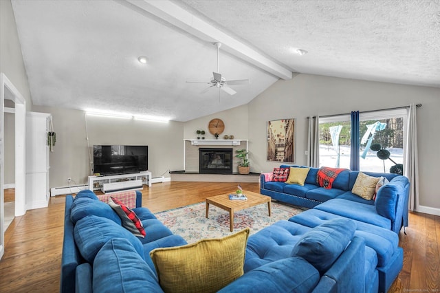 living area with vaulted ceiling with beams, a textured ceiling, wood finished floors, and a glass covered fireplace