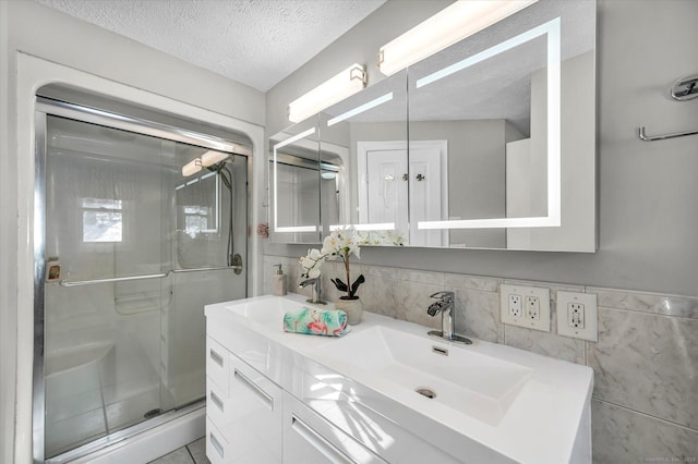 bathroom with double vanity, a stall shower, a textured ceiling, and a sink