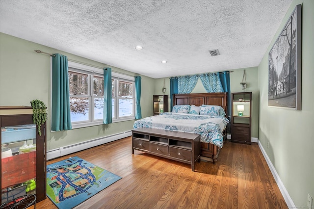 bedroom featuring baseboards, visible vents, a baseboard heating unit, and wood finished floors