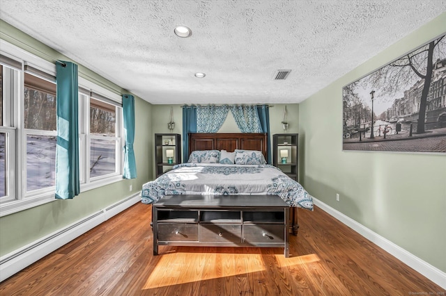 bedroom featuring visible vents, baseboards, wood finished floors, a textured ceiling, and a baseboard heating unit