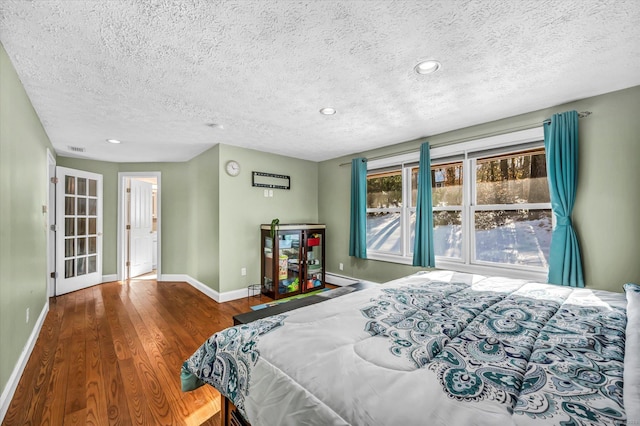 bedroom featuring visible vents, a baseboard heating unit, a textured ceiling, wood finished floors, and baseboards