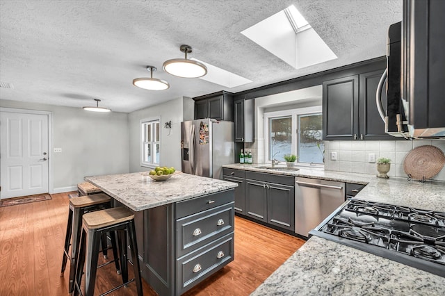 kitchen featuring a skylight, a center island, light wood finished floors, stainless steel appliances, and a sink