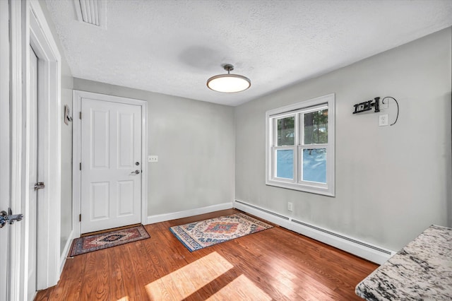 foyer with a textured ceiling, a baseboard heating unit, wood finished floors, visible vents, and baseboards