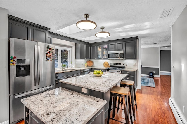 kitchen with a baseboard radiator, appliances with stainless steel finishes, a kitchen island, a sink, and wood finished floors