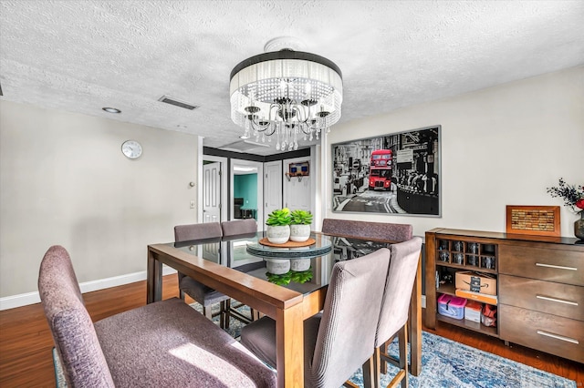 dining room featuring baseboards, visible vents, wood finished floors, a textured ceiling, and a notable chandelier