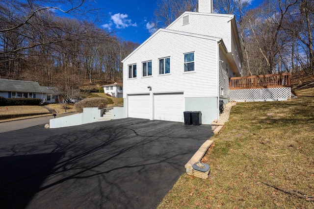 view of side of home with a garage, a chimney, aphalt driveway, and a lawn