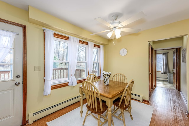 dining room with a baseboard radiator, light wood-style flooring, and baseboards