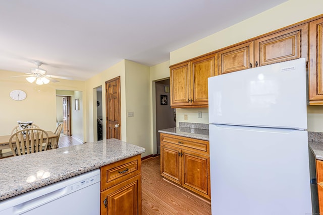 kitchen with brown cabinets, light wood-style flooring, ceiling fan, light stone countertops, and white appliances