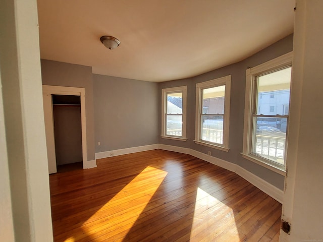 unfurnished bedroom with hardwood / wood-style flooring, multiple windows, baseboards, and a closet