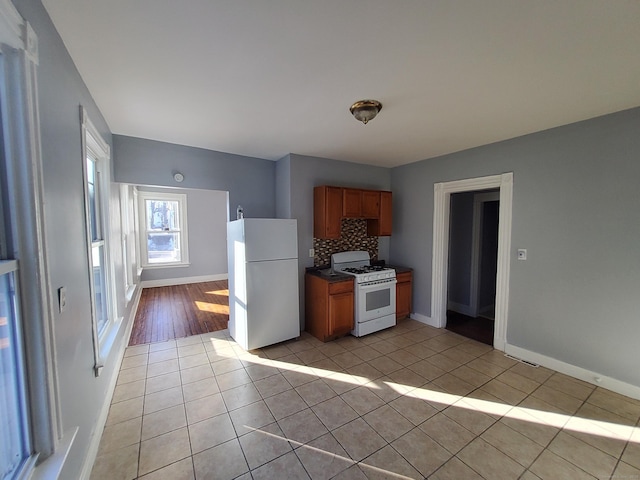 kitchen with brown cabinets, light tile patterned floors, tasteful backsplash, white appliances, and baseboards