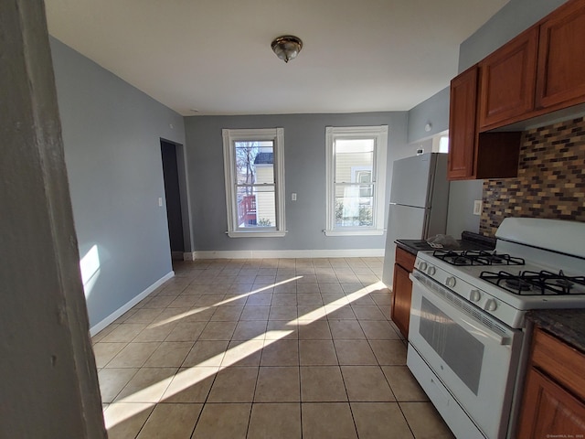 kitchen featuring gas range gas stove, light tile patterned floors, dark countertops, decorative backsplash, and baseboards