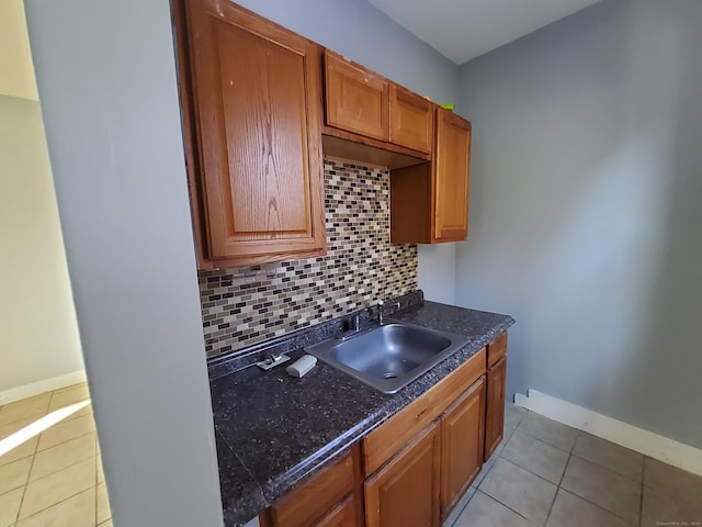 kitchen featuring light tile patterned floors, baseboards, dark countertops, a sink, and backsplash