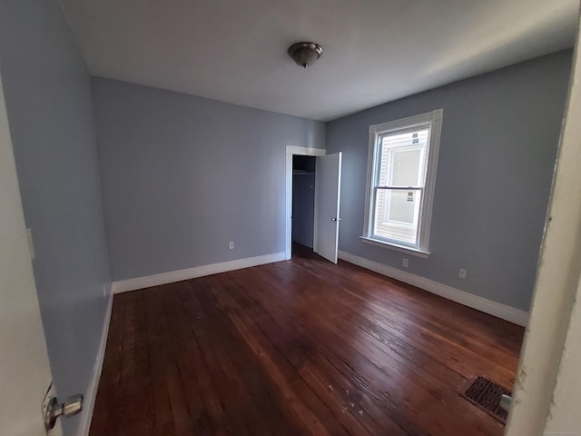 unfurnished bedroom with a closet, dark wood finished floors, visible vents, and baseboards