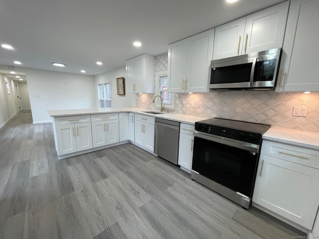 kitchen featuring a peninsula, stainless steel appliances, light wood-type flooring, white cabinetry, and a sink