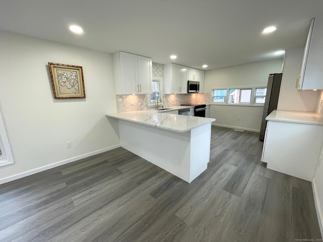 kitchen with dark wood-style flooring, tasteful backsplash, appliances with stainless steel finishes, a sink, and a peninsula