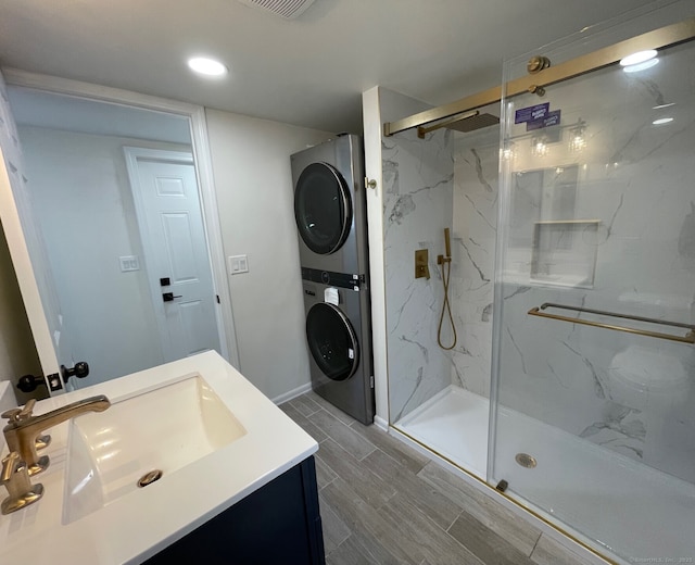 bathroom with a marble finish shower, baseboards, stacked washer / drying machine, wood tiled floor, and vanity