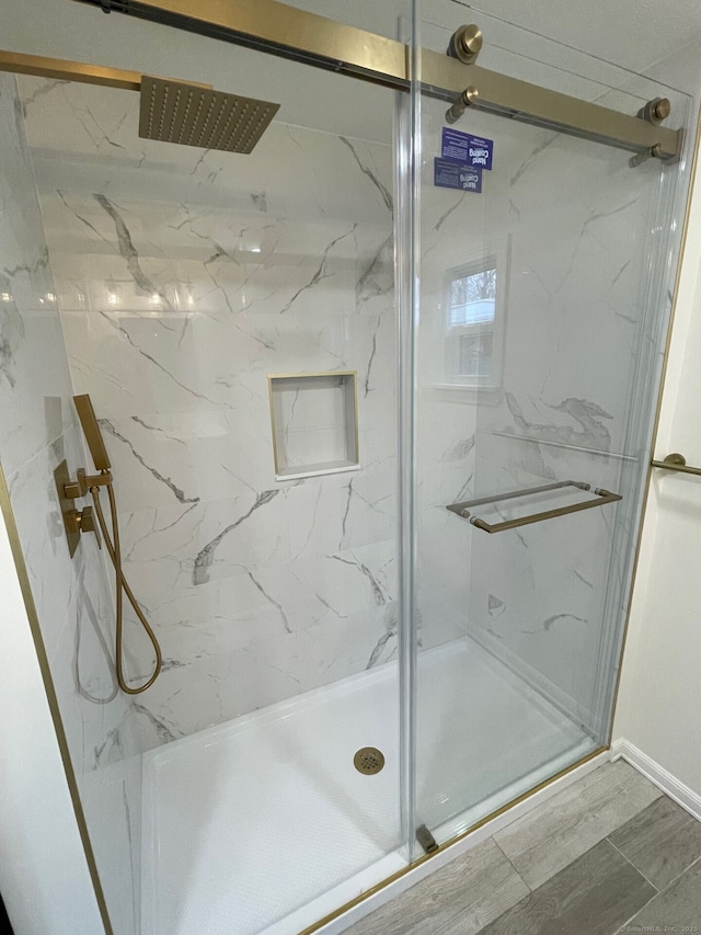 full bathroom with a marble finish shower and wood finished floors