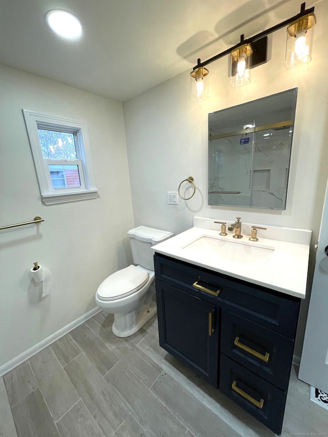 bathroom featuring baseboards, toilet, vanity, and a marble finish shower